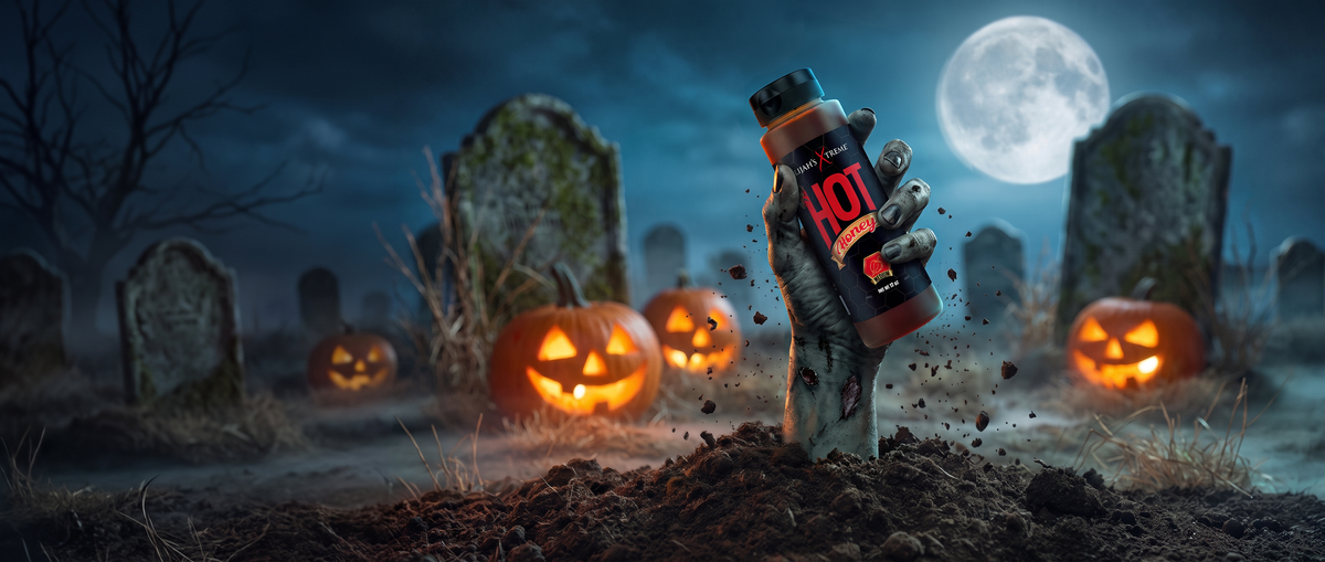 A hand holding a bottle of Elijah's Xtreme Ghost Pepper hot sauce above a field of chili peppers